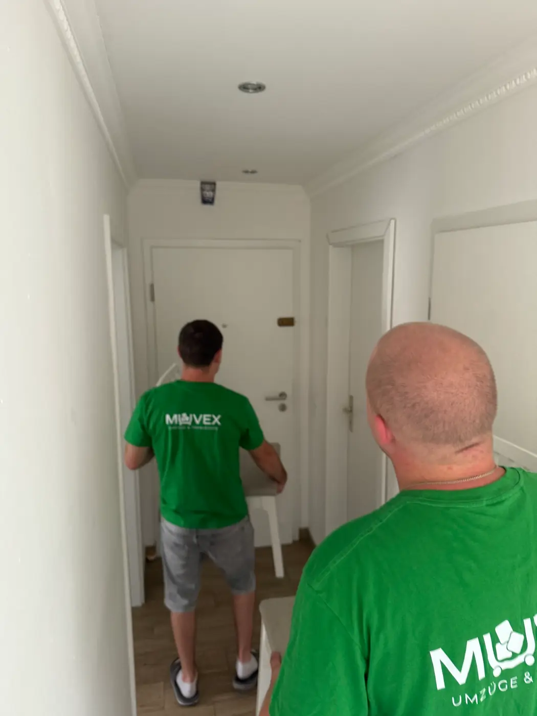 Zwei Muvex-Mitarbeiter tragen Umzugsgut durch den Flur einer leeren Wohnung