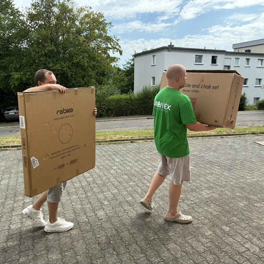 Zwei Muvex-Mitarbeiter tragen einen großen Karton zum Transporter