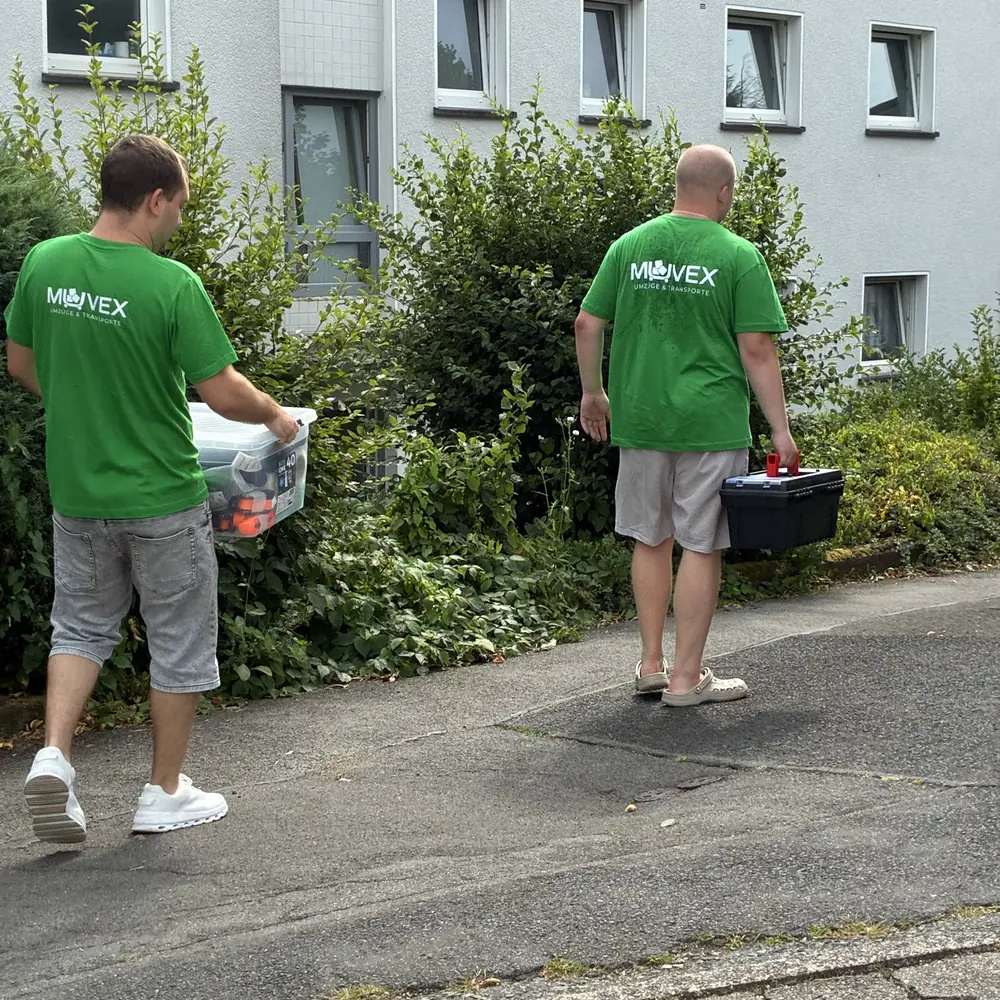 Zwei Muvex-Mitarbeiter mit Werkzeug und Karton auf dem Weg zum Kunden