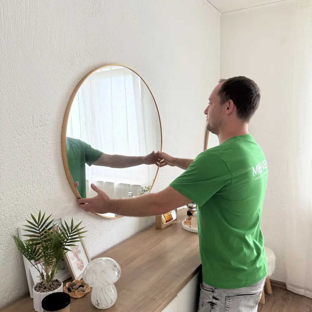 Muvex-Mitarbeiter hängt in der neuen Wohnung einen Spiegel auf