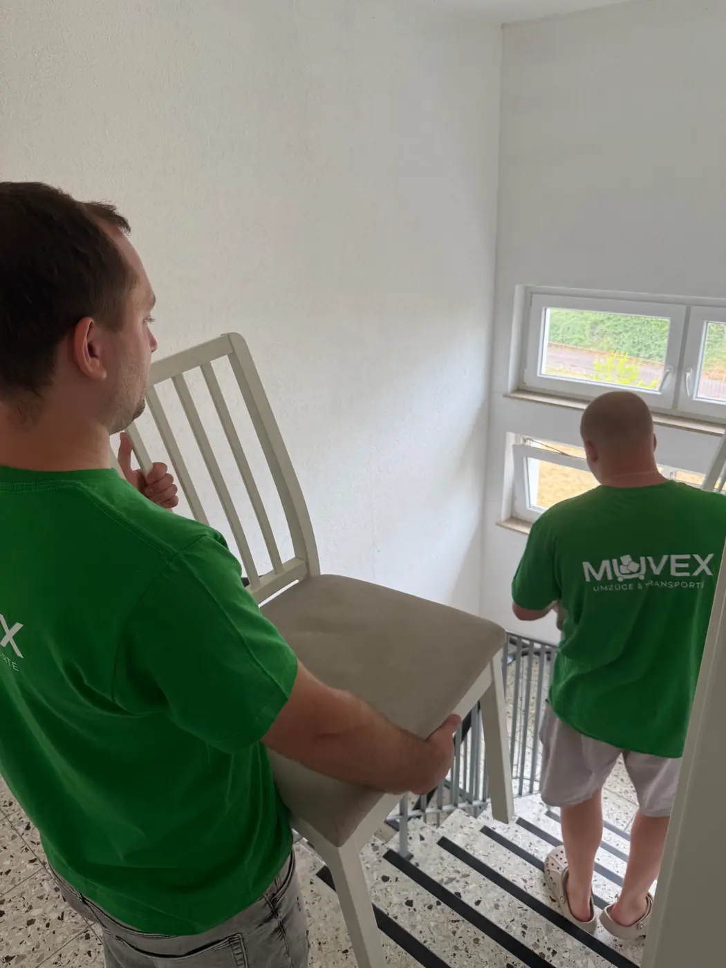 Zwei Muvex-Mitarbeiter tragen Stühle durchs Treppenhaus